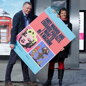 Two members of the cultural scene in Edinburgh holding an over-sized poster of Andy Warhol exhibition